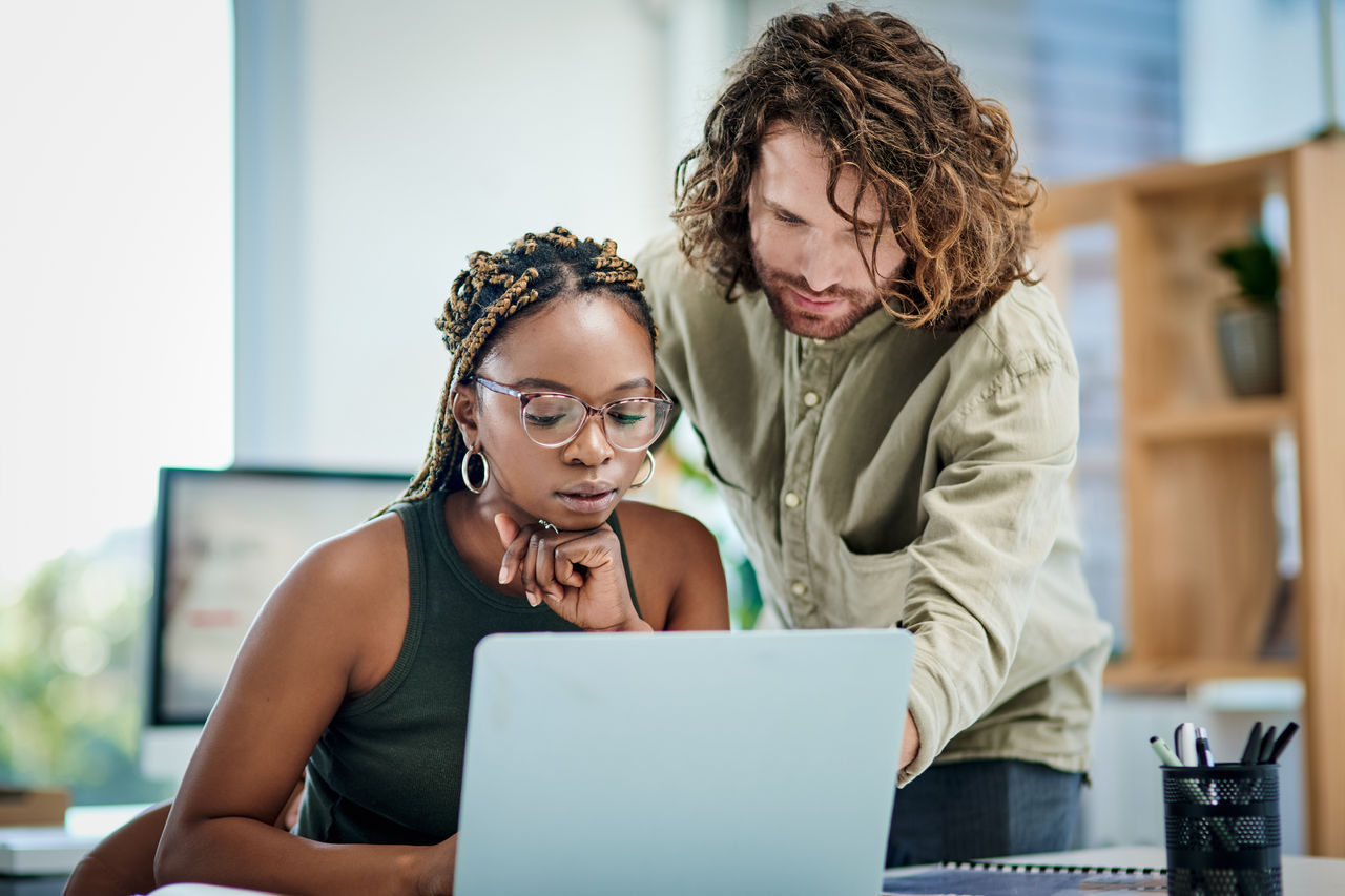 Two developers on laptop in office both looking at screen intently